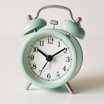Soft pastel twin-bell alarm clock on a linen bedside table